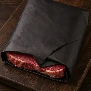 Steak wrapped in heavy black meat saver paper on a wooden board