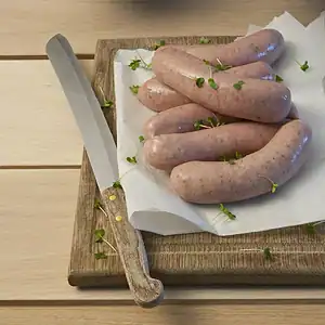 Sausages filled in hog casing, resting on parchment on a wooden board beside a knife