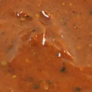 Close-up of RAPS Chilli Willy marinade, a red-brown paste with whole peppercorns and chilli seeds