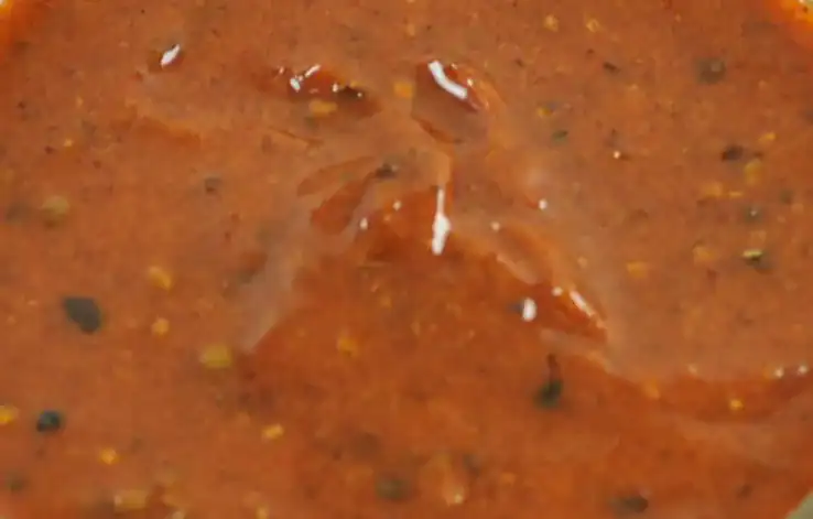 Close-up of RAPS Chilli Willy marinade, a red-brown paste with whole peppercorns and chilli seeds